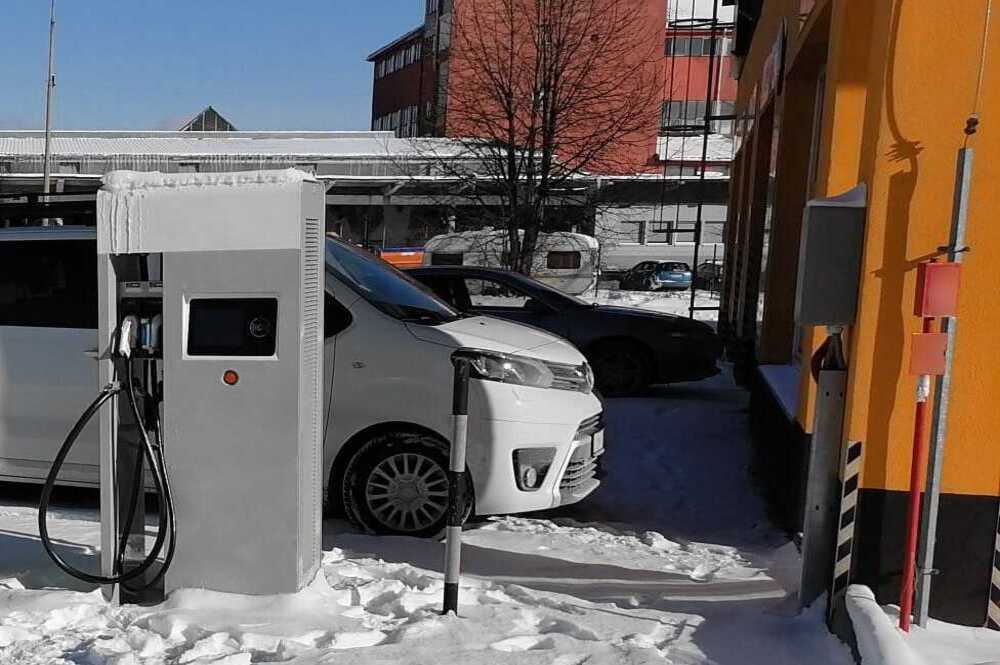 Vehículo eléctrico conectado a un cargador en un paisaje nevado, afectado por el clima en el rendimiento de las baterías.